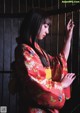 A woman in a red kimono standing in front of a window.