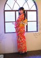 A woman in a red kimono standing in front of a window.