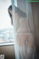 A woman in a white lingerie standing by a window.