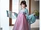 A woman in a pink and blue hanbok is posing for a picture.