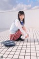 A young woman in a school uniform crouching on the ground.