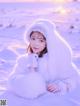 A young girl in a white fur coat sitting in the snow.