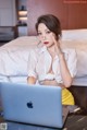 A woman sitting on a bed with a laptop computer.