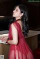 A woman in a red dress leaning against a counter.