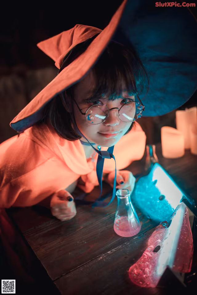 A little girl in a witches hat and glasses sitting at a table.