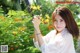 A woman in a white shirt holding a yellow flower.