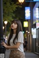 A woman leaning against a lamp post on a city street.