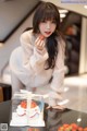 A woman in a white sweater holding a strawberry in front of a cake.