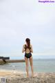 A woman in a black bathing suit standing on a rock by the ocean.