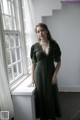 A woman in a green dress standing by a window.