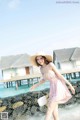 A woman in a pink dress and straw hat walking on the beach.