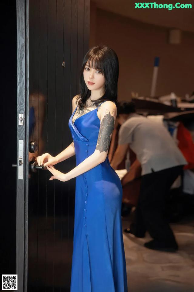 A woman in a blue dress standing in front of a door.