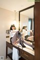 A woman sitting on top of a dresser in front of a mirror.