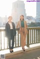 Two young women standing next to each other on a bridge.