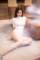 A woman in a white bodysuit sitting on the floor.