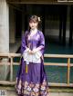 A woman in a purple hanbok standing next to a body of water.