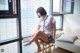 A woman sitting on a stool in front of a window.