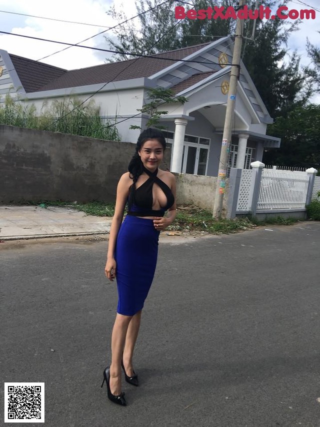 A woman in a blue dress standing on the side of a road.