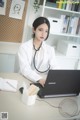 A woman in a white lab coat sitting at a desk with a laptop.