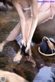 A woman in a pink dress is putting on her shoes in the water.