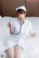 A woman dressed as a nurse sitting on a bed with a stethoscope.