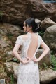 A woman in a white dress standing in front of rocks.