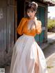 A woman in an orange shirt and white skirt posing for a picture.