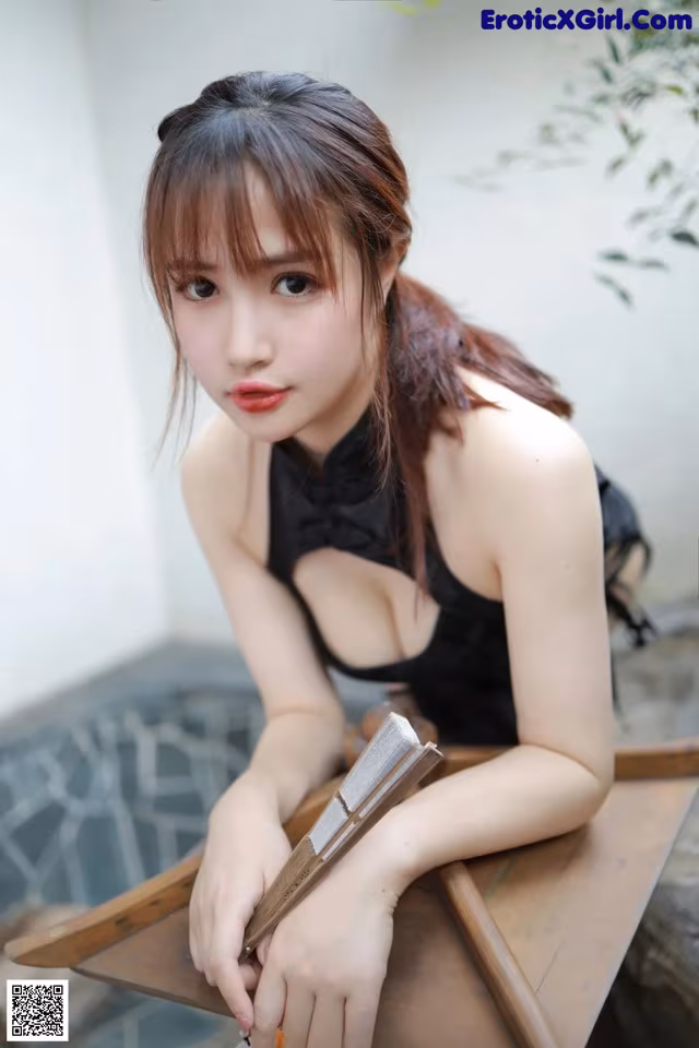 A woman in a black dress sitting on a wooden table.