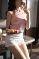 A woman in a pink top and white shorts eating a piece of fruit.